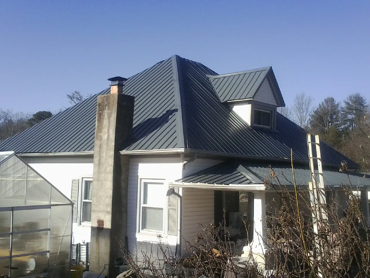 Dark blue standing seam metal roof on a white farmhouse with dormer — Slate & Tile Roof Repair by Roofing Brothers in Farnham