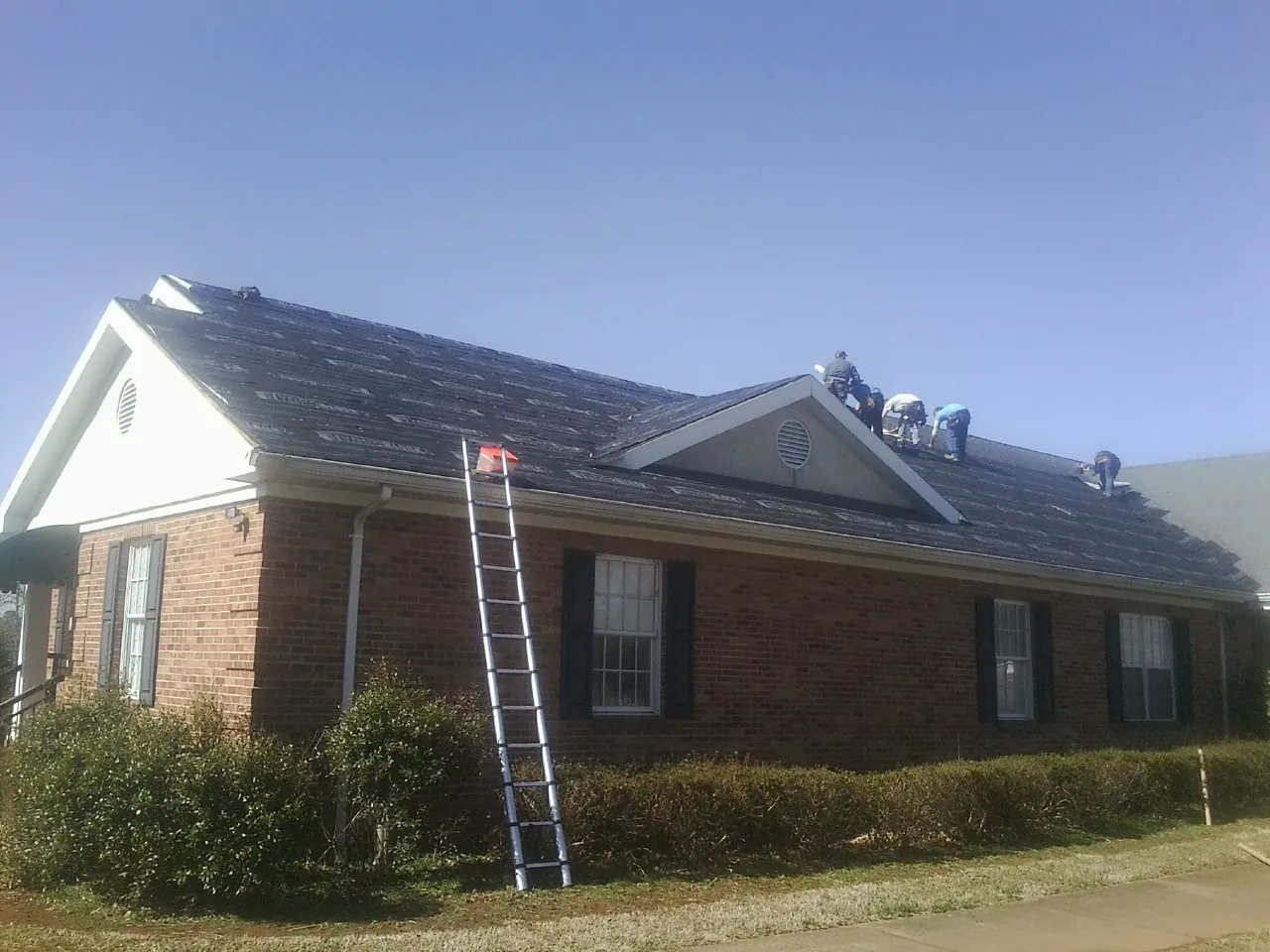 Crew tearing shingles off a brick ranch roof with a ladder set — Emergency Roof Repair work by our crew in Farnham