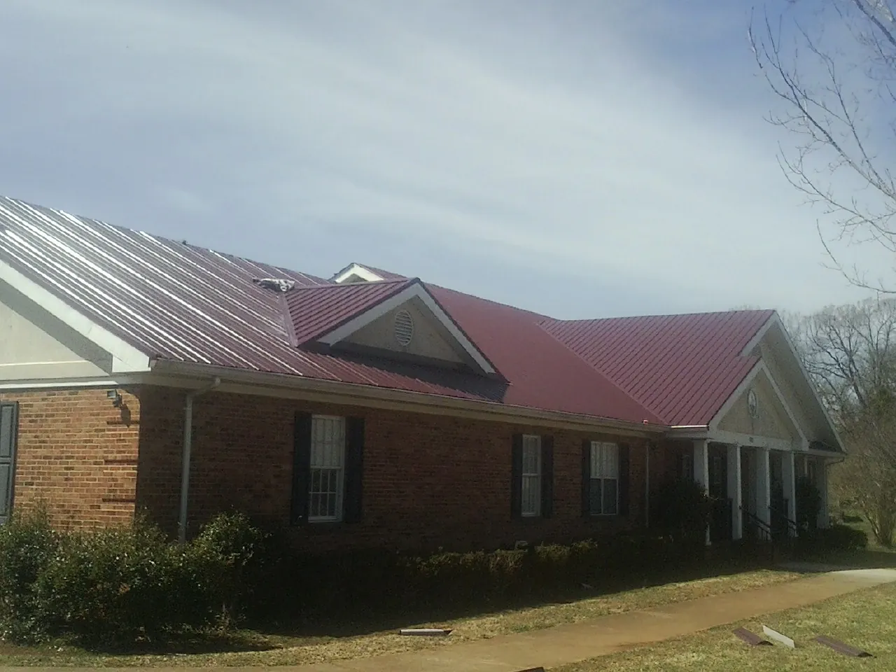 Red metal roof with gabled entries on a long brick building, from a Hail Damage Roof Repair job in Farnham