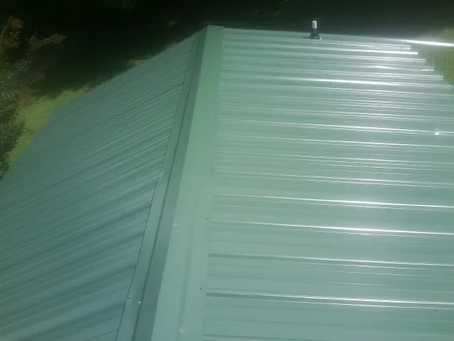 New green metal panels meeting at the ridge of a roof — Flat Roof Repair work by our crew in Farnham