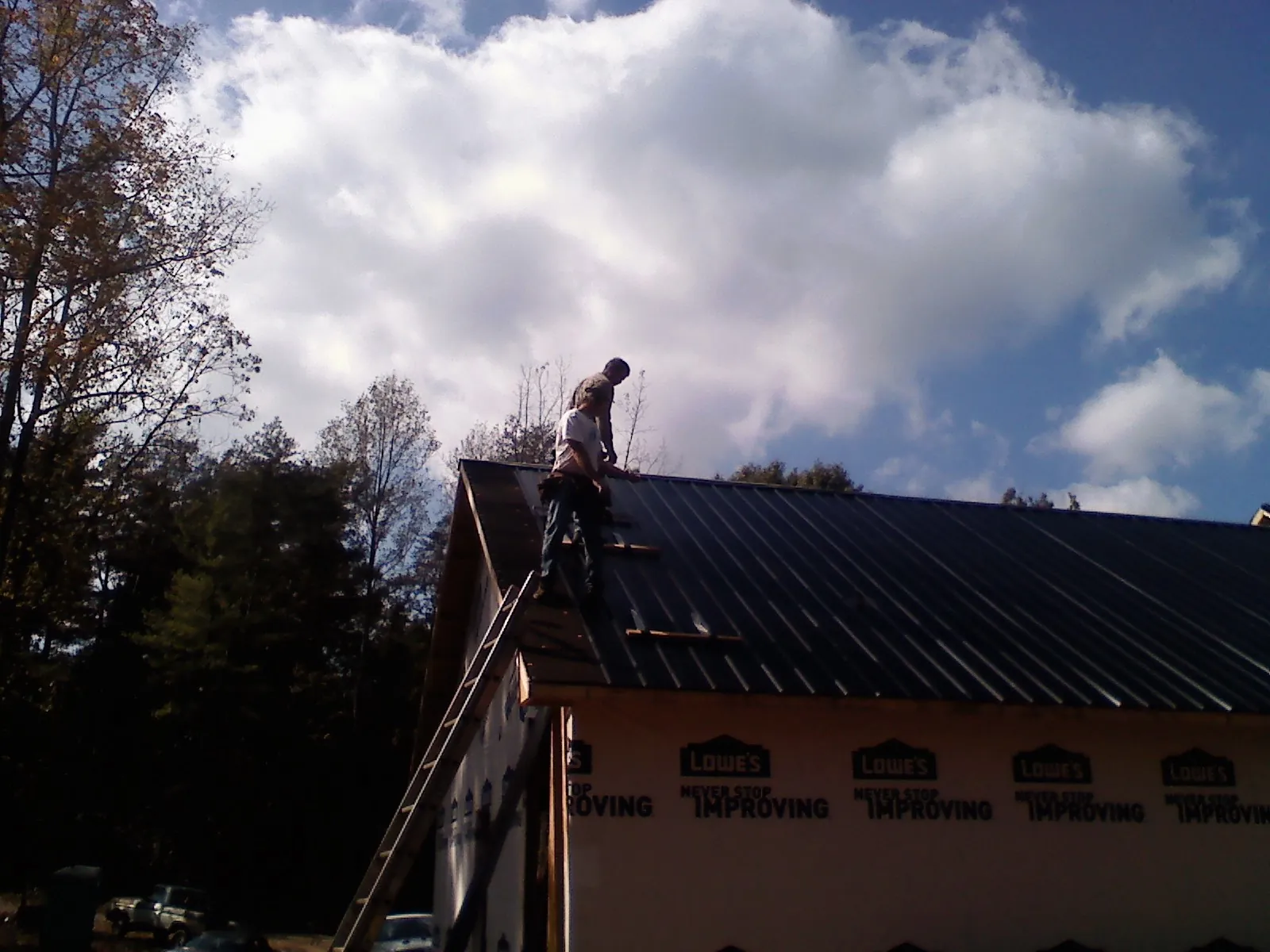 Roofer fastening dark metal panels high against a cloudy sky, from a Roof Inspection job in Farnham