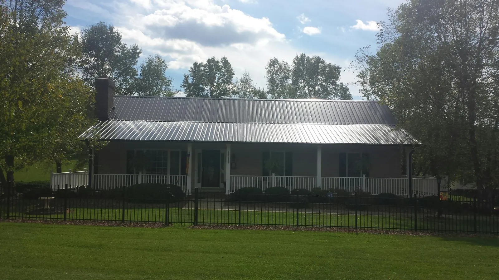 Gray metal roof on a brick ranch with a full width front porch — Gutter Guard Installation work by our crew in Farnham