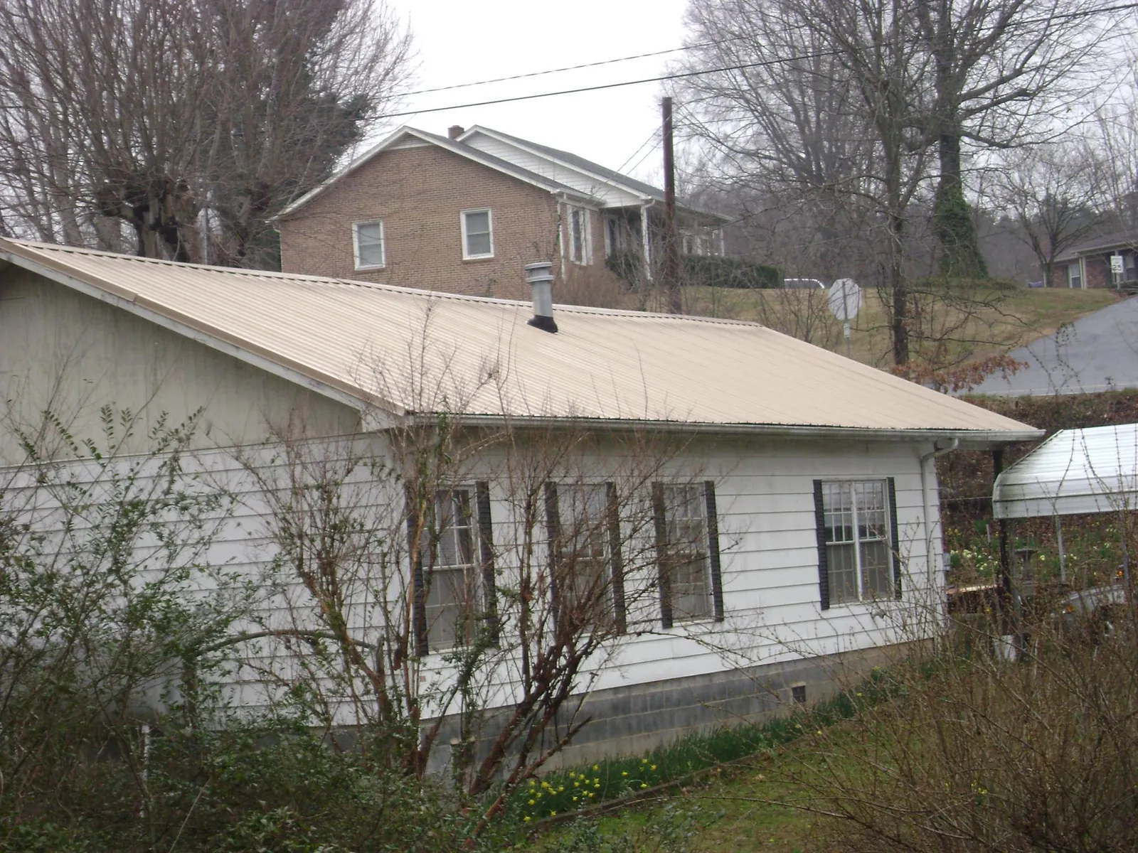 Tan metal roof on a white sided house set into a hillside — Commercial Roofing by Roofing Brothers in Farnham